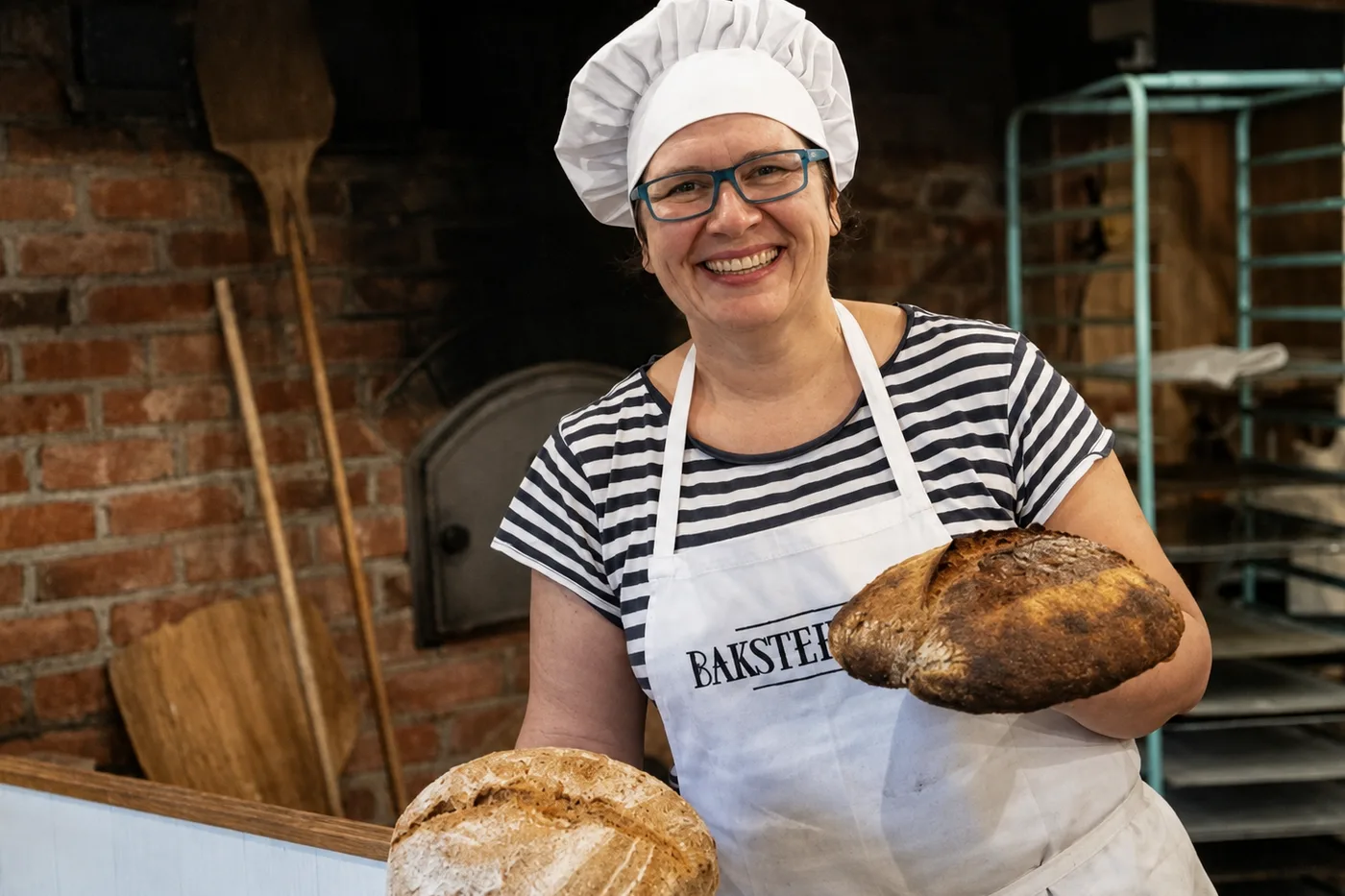 Mariann holding two finished sourdough loaves in front of the wood-fired oven