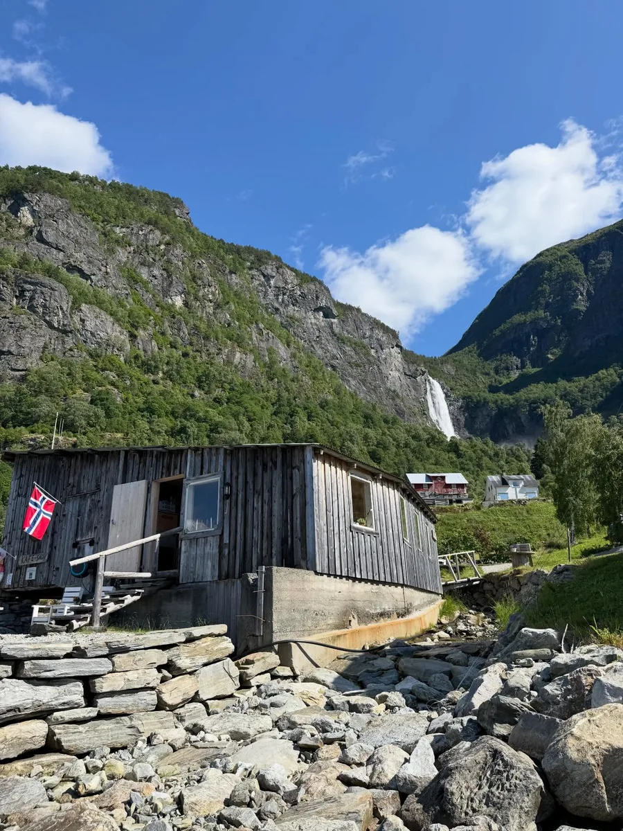The grey timber sawmill building with Feigefossen falling down the mountain behind it