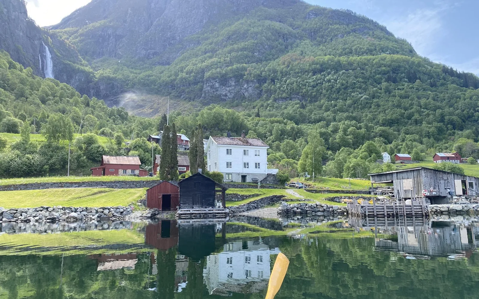 The farm at Feigum seen from the water, with Feigefossen falling down the mountainside behind it
