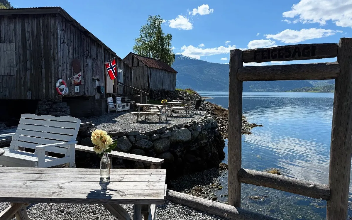 The sign, the benches and Lustrafjorden in sunshine outside the old sawmill