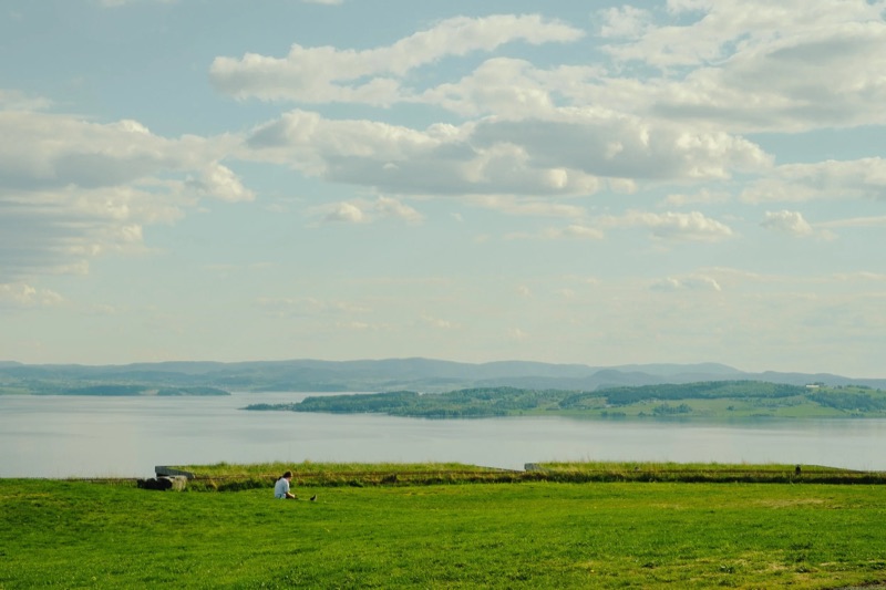 A guest sitting in the grass above the turf roofs, the fjord beyond