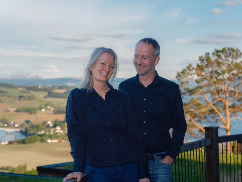 Kristine and Frode Sakshaug on the terrace, farmland and fjord behind them