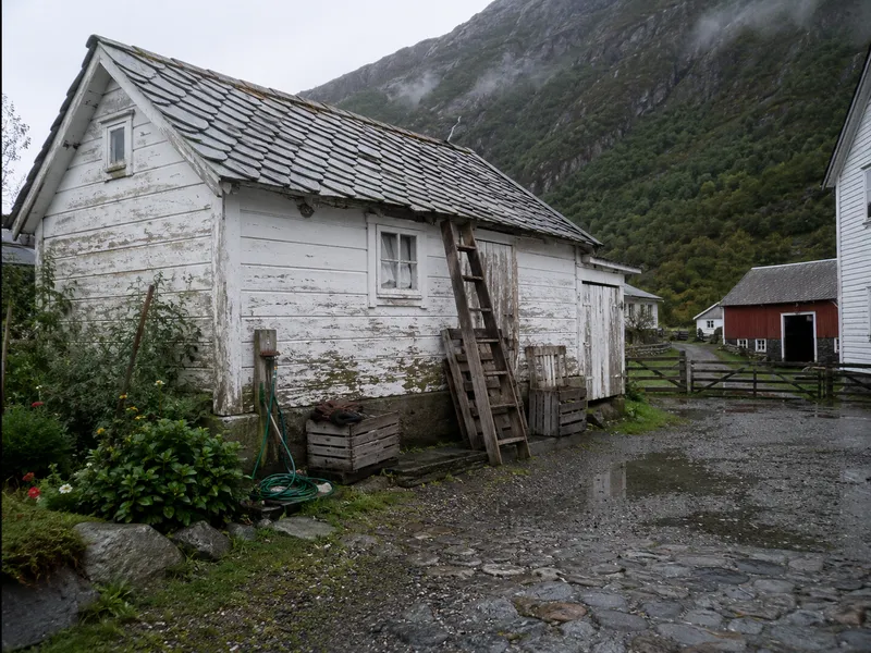 Hvitmalt uthus med skifertak, stige og tomme fruktkasser mot veggen etter regn