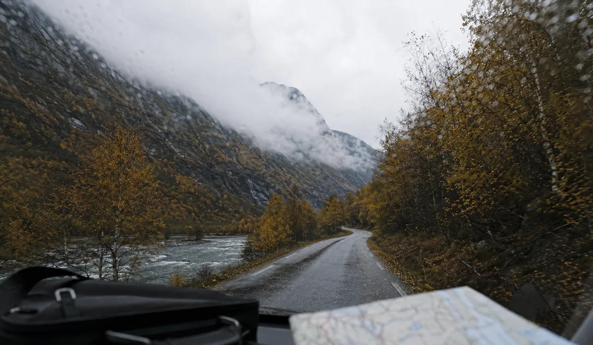 A wet valley road in autumn seen through a windscreen, camera bag and map on the dashboard
